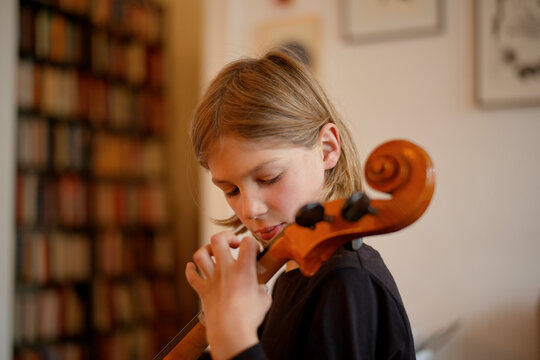 Young boy focused while playing the violin indoors with paintings in the background.