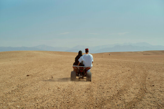 Two people on an ATV riding through a vast desert landscape under a clear sky.