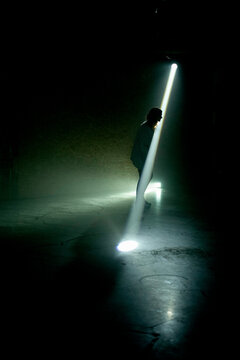 Silhouette of a person standing in a dark tunnel illuminated by a shaft of light from above.