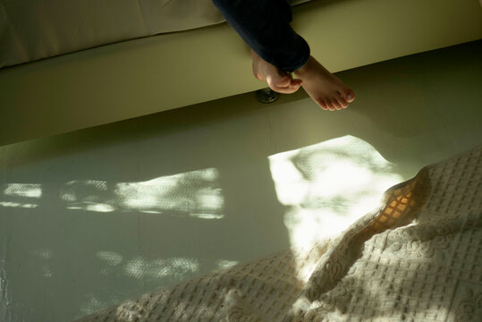 Bare feet dangle over a white couch above a cream textured rug with sunlit patterns casting shadows on it.
