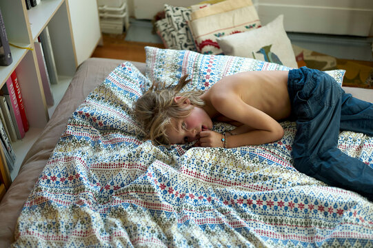 Young child rests on a vibrant quilted bed, looking pensive.