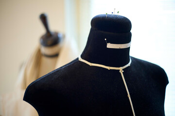 Black dress form with measuring tape on the neck, pins on top, and a blurred background featuring a kitchen knife block.