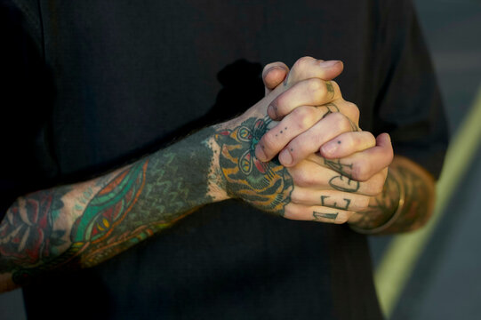 Close-up of a person's clasped hands showing intricate tattoo designs on the forearms.