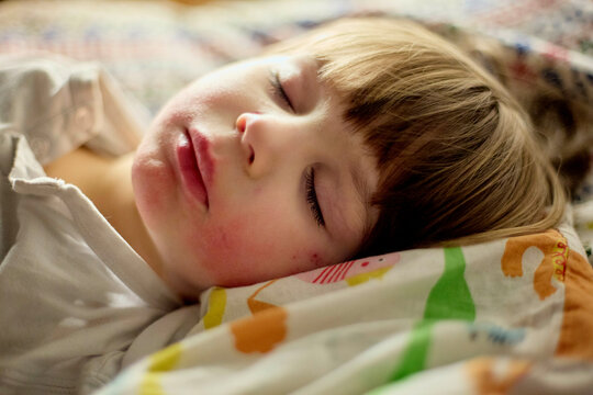 Young child sleeps peacefully on a colorful pillow with eyes closed and a serene expression.