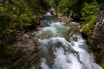 Obraz premium Vintgar Gorges Park a few km from Lake Bled, Slovenia. Wooden walkways accompany the path above the river rapids and waterfalls. River hits rocks and creates fog.Adventure family holidays. Freshness.