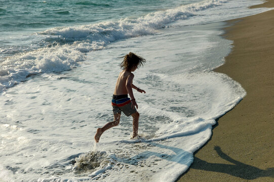 Young child runs along the shoreline with waves crashing near their feet on a sunny beach day.