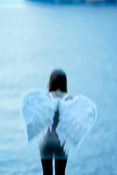 A blurred figure with angel wings stands facing away from the camera against a blue backdrop.
