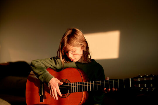 A contemplative young person with a guitar bathed in warm sunlight.