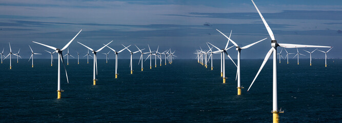Offshore wind turbines standing tall in a blue sea against a clear sky.