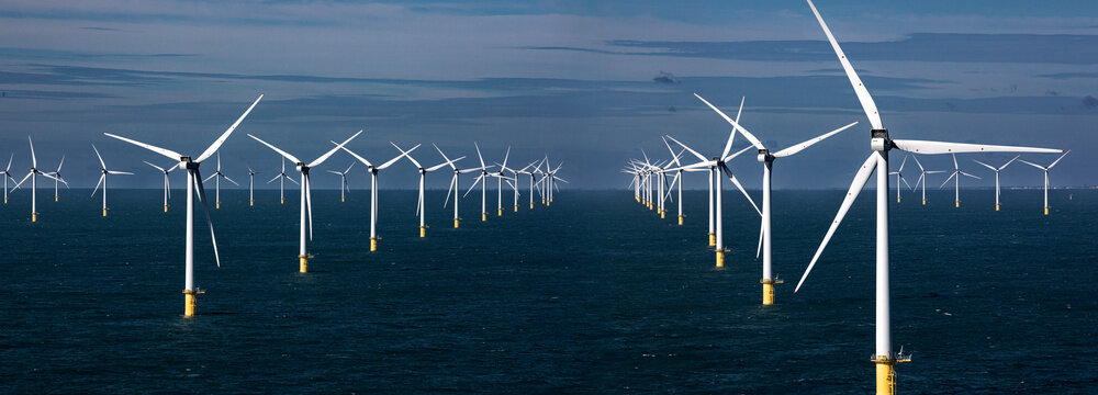 Offshore wind turbines standing tall in a blue sea against a clear sky.
