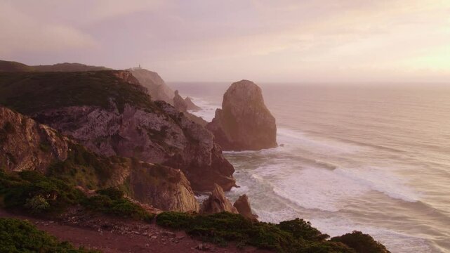 Aerial view of cliff, beach, ocean, rocks, waves at Praia do Caneiro during sunset, Cabo da Roca, Colares, Portugal.