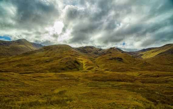 Dramatic view of rolling hills under a cloudy sky with patches of sunlight highlighting the landscape's texture.