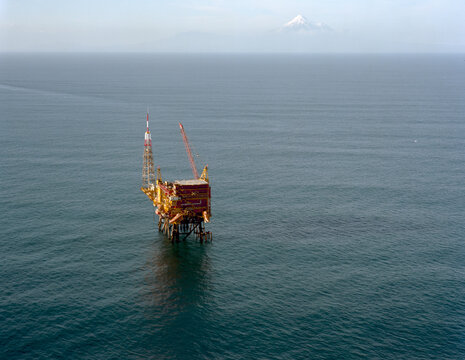 An offshore drilling platform stands in the middle of the ocean with a distant mountain visible on the horizon under a clear sky, Tasman Sea, New Zealand