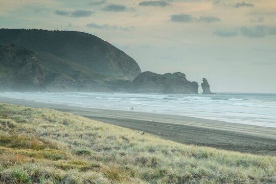 Misty ocean beach with grassy dunes and a rocky outcrop in the distance.