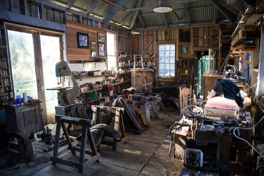 Interior view of a rustic and cluttered woodworking workshop with tools, wooden planks, and a bandsaw, Auckland, New Zealand