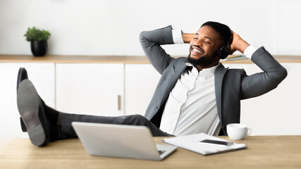 Don't worry be happy. Handsome black businessman in headphones listening his favorite music at workplace in modern office, panorama