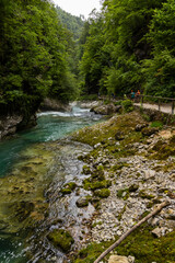 Fototapeta premium Vintgar Gorges Park a few km from Lake Bled, Slovenia. Wooden walkways accompany the path above the river rapids and waterfalls. River hits rocks and creates fog.Adventure family holidays. Freshness.