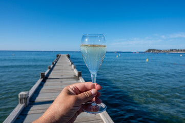 Summer time in Provence, hand with glass of cold champagne cremant sparkling wine on famous Pampelonne sandy beach near Saint-Tropez in sunny day, Var department, France, beach club party