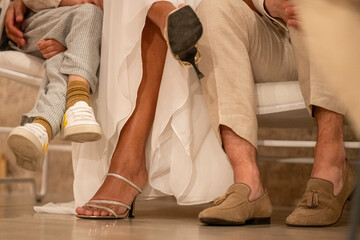 Wedding guests seated with a focus on their contrasting footwear, including a pair of strappy sandals, sneakers, and suede shoes.