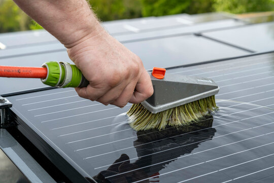 Close-up of a hand cleaning a solar panel with a brush to ensure efficient energy absorption.