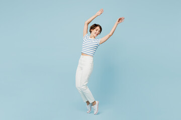 Obraz premium Full body side view young woman wears striped t-shirt casual clothes leaning back raise up hands stand on toes dance isolated on plain pastel light blue background studio portrait. Lifestyle concept.