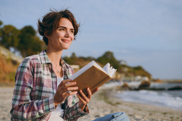 Side profile view young fun happy dreamful woman wear shirt casual clothes reading paper book novel...