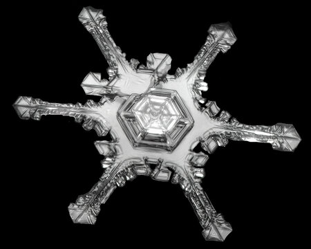 Close-up of a single snowflake showcasing intricate patterns and symmetry in monochrome.