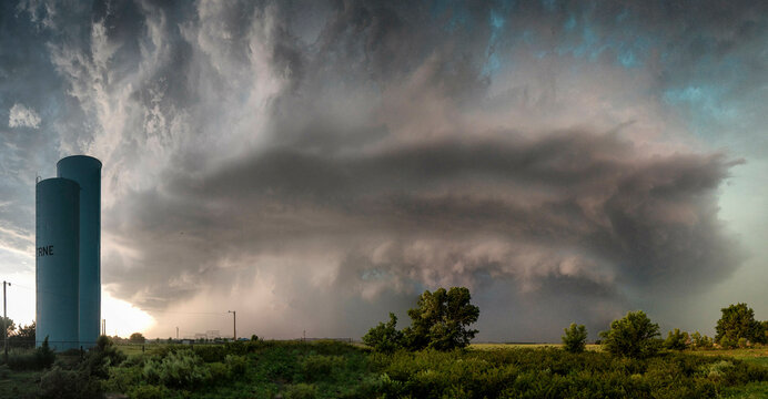 A dramatic storm cloud looms over a rural landscape with a blue water tower standing tall against the turbulent sky.