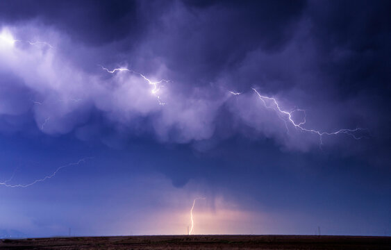 Lightning bolts illuminate the night sky above a flat landscape.