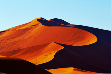 A vibrant image capturing the smooth curves and rich orange hues of sand dunes under a clear sky at dusk or dawn.
