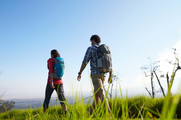 Two hikers with backpacks walking through a grassy field with a clear blue sky above them.