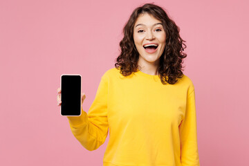 Young happy student woman she wearing yellow sweatshirt casual clothes hold in hand use mobile cell phone with blank screen workspace area isolated on pastel light pink background. Lifestyle concept.