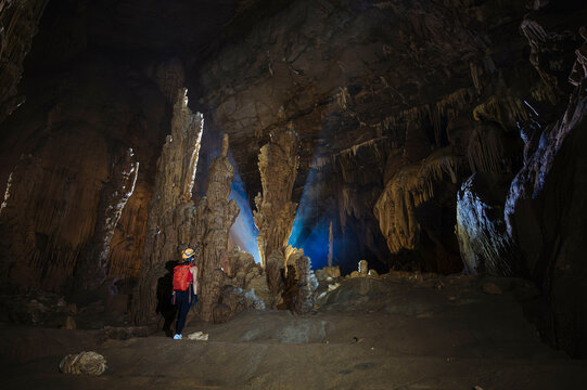 A person explores a vast cave with impressive stalactites and stalagmites illuminated by natural light.
