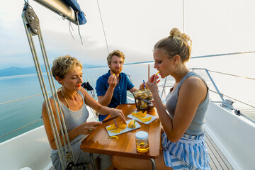 Group of friends enjoying a meal on a sailboat at sunset with calm seas in the background