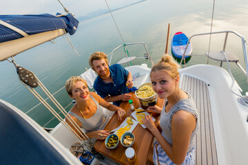 Group of friends enjoying snacks and drinks on the deck of a yacht at sea during a sunny day.
