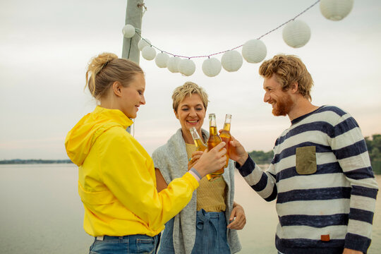 Three friends enjoying a beachside party with festive lights and a toast at sunset.