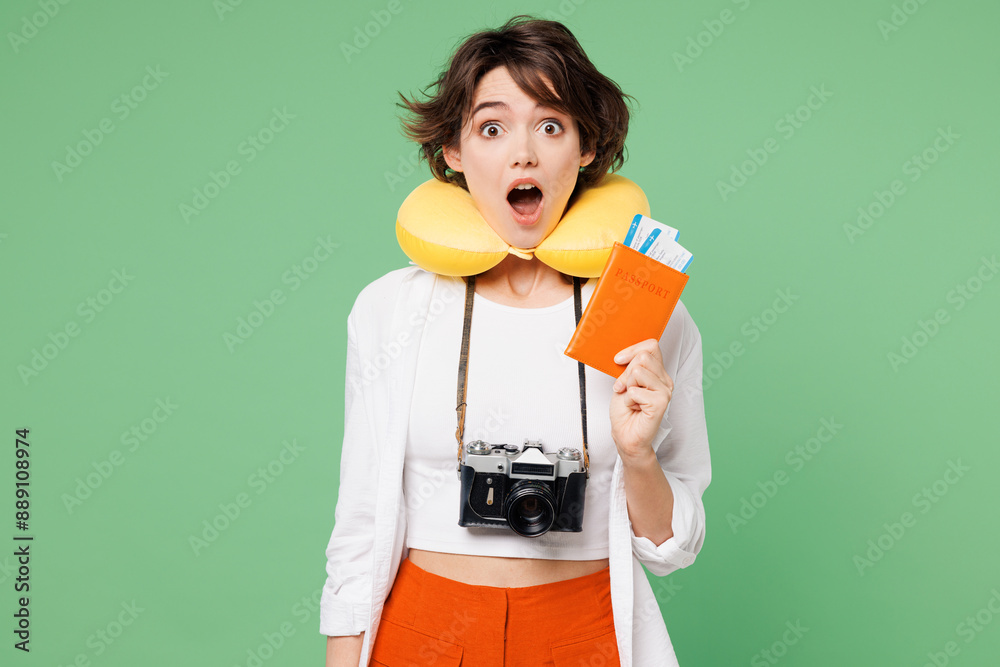 Wall mural Traveler surprised woman wear casual clothes neck pillow hold passport ticket look camera isolated on plain green background. Tourist travel abroad in free time rest getaway. Air flight trip concept.