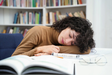 Tired female architect working in library with blueprints and falling asleep