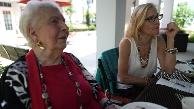 Mature woman and elderly woman or grandmother sit at outdoor cafe talking, smiling and laughing.