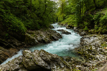 Fototapeta premium Vintgar Gorges Park a few km from Lake Bled, Slovenia. Wooden walkways accompany the path above the river rapids and waterfalls. River hits rocks and creates fog.Adventure family holidays. Freshness.