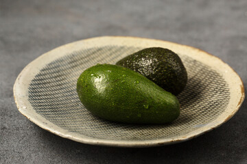 Two avocado fruits on a gray clay plate made by hand on a gray background