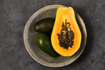 Two avocados and half a papaya on a gray clay plate