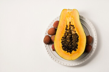Half of a beautiful juicy ripe papaya and lychee on a white plate on a white table