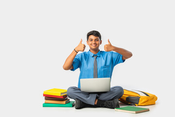 Asian Indian schoolboy with books and laptop, pointing at blank space, promoting education
