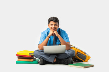 Asian Indian schoolboy with books and laptop, pointing at blank space, promoting education