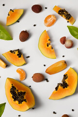 Fruit background made of pieces of ripe papaya, tangerine and litchi on a white background