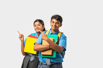 Asian Indian schoolboy and schoolgirl in uniforms, presenting blank space with books and backpacks