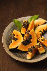 Sliced ​​ripe papaya in a handmade ceramic bowl on a wooden table