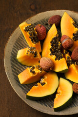 Sliced ​​ripe papaya with lychee in a handmade ceramic bowl on a table