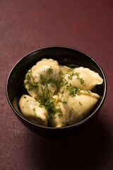 A bowl of potato dumplings with butter and dill on a burgundy background